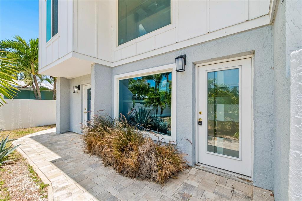 A paved patio sits in front of a white building with a glass-paneled door — 970 BOCA CIEGA ISLE DRIVE, ST PETE BEACH, FL