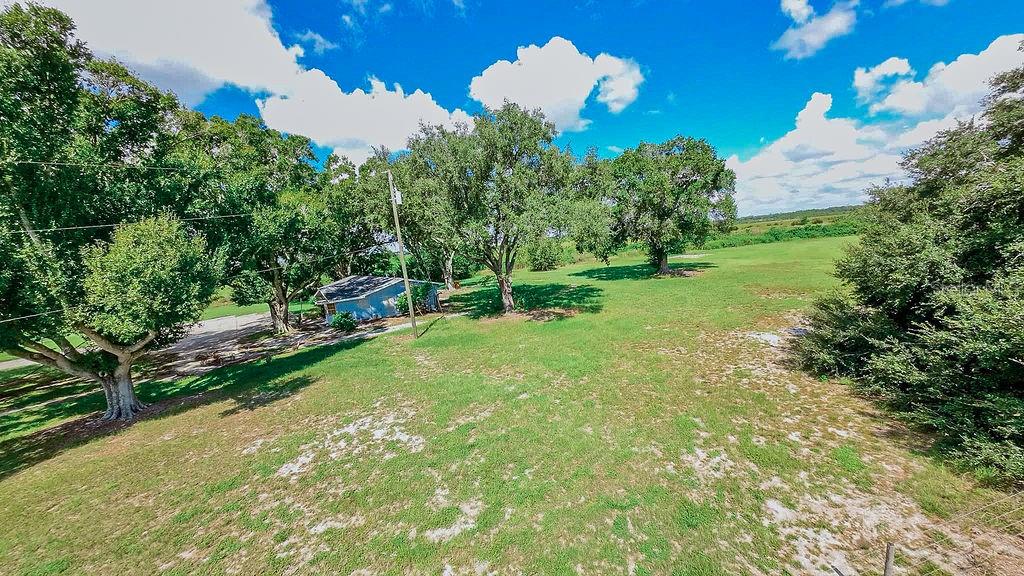 An aerial view shows a grassy lot with several large trees and a small blue house — 1030 CHALET SUZANNE ROAD, LAKE WALES, FL