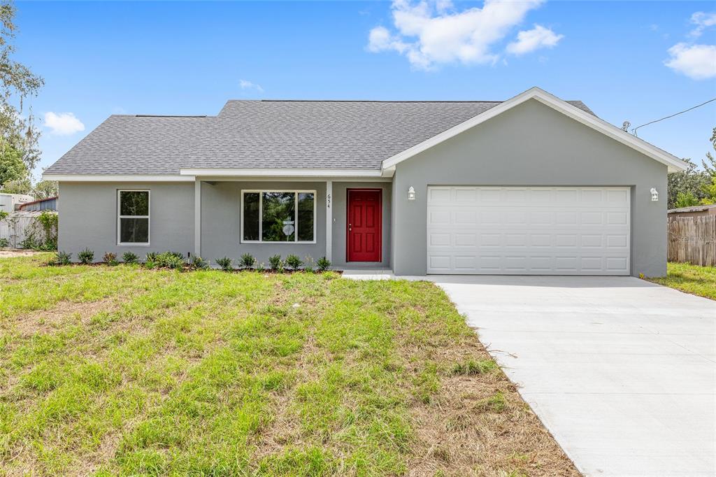 A gray single-story house features a red front door, a white garage, and a lawn — 654 NE 130TH COURT, SILVER SPRINGS, FL