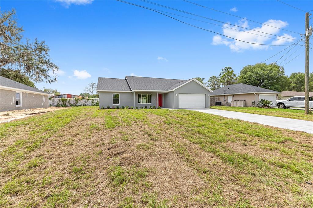 A single-story gray house with a white garage and a large, patchy grass front yard — 654 NE 130TH COURT, SILVER SPRINGS, FL