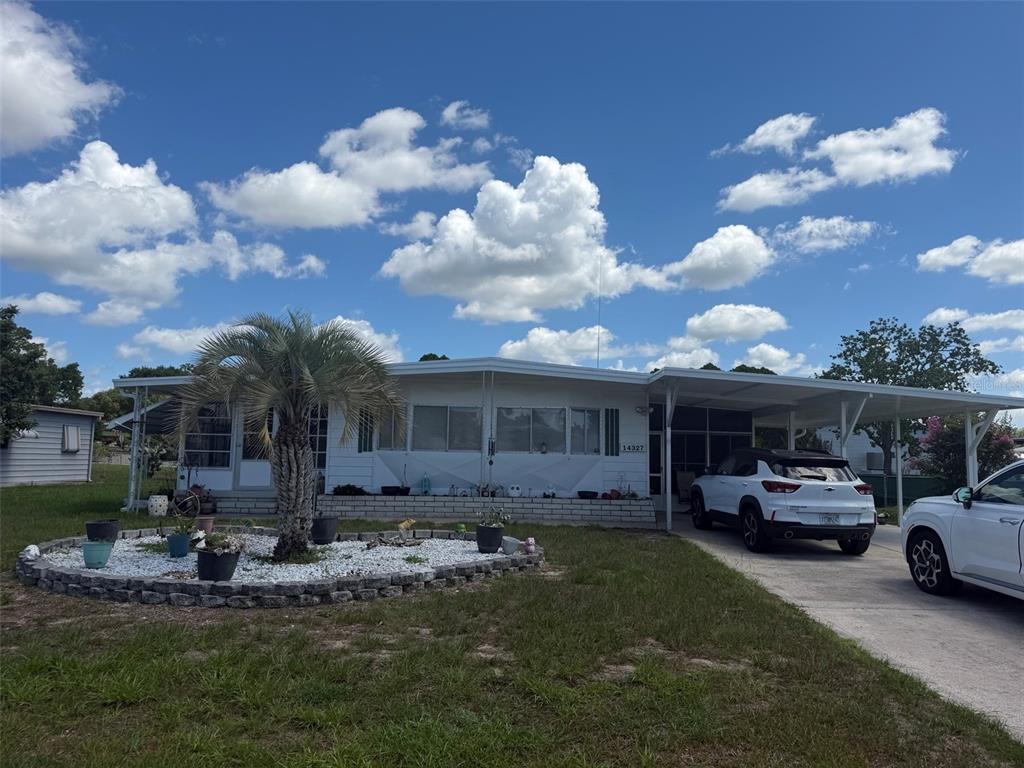 A white mobile home with a palm tree, a circular garden, and a covered carport — 14327 EVERMORE STREET, BROOKSVILLE, FL