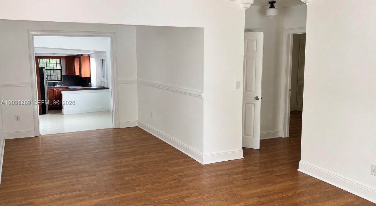 An interior view shows a room with wood-look flooring, white walls, and a kitchen beyond — 325 NW 56th St, Miami FL 33127, MIAMI, FL