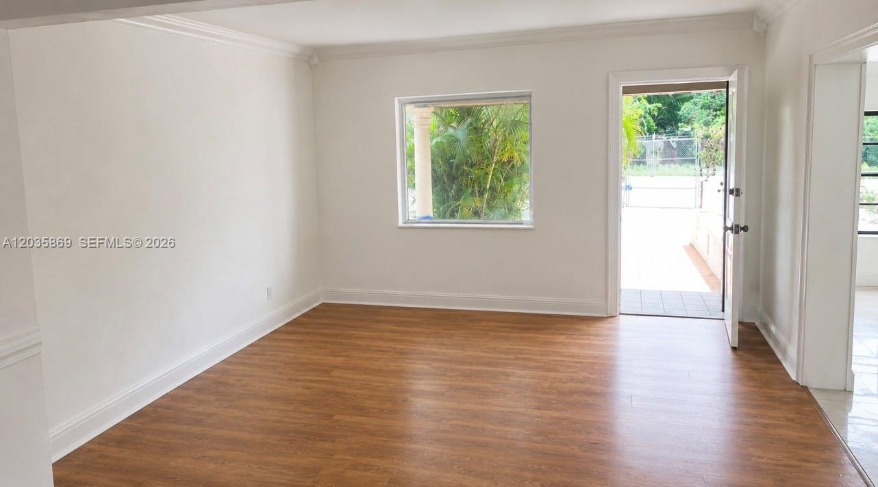 An empty room features wood-look flooring, white walls, a window, and an open exterior door — 325 NW 56th St, Miami FL 33127, MIAMI, FL