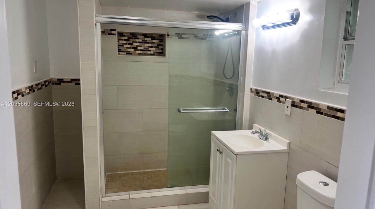 A bathroom features a glass-enclosed shower, a white vanity, and decorative tile accents — 325 NW 56th St, Miami FL 33127, MIAMI, FL