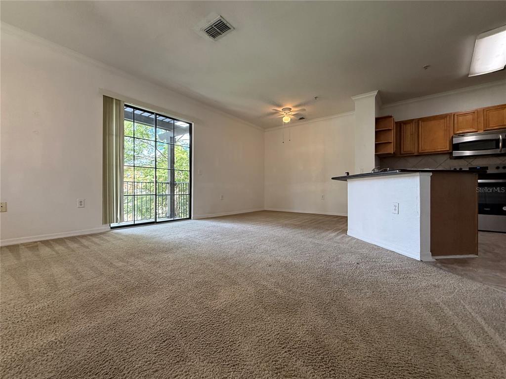 A carpeted living room features a sliding glass door and an open kitchen island — 6121 METROWEST BOULEVARD UNIT 101, ORLANDO, FL
