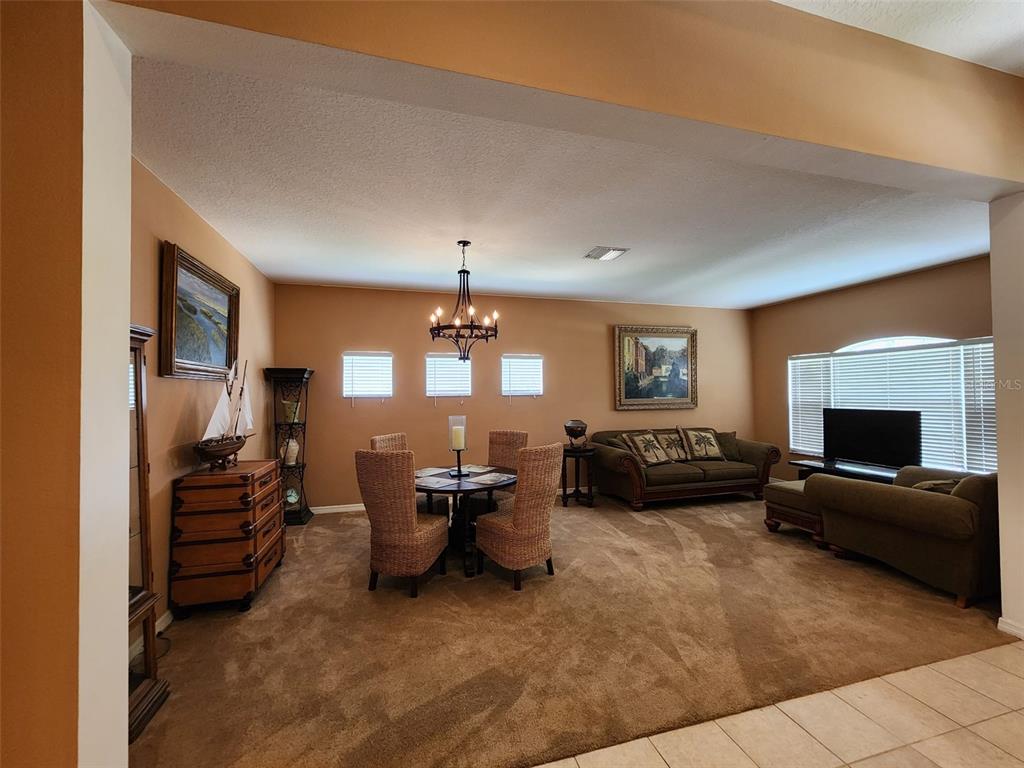 A dining area and living room with brown carpet, tan walls, and a chandelier — 1829 MIRA LAGO CIRCLE, RUSKIN, FL