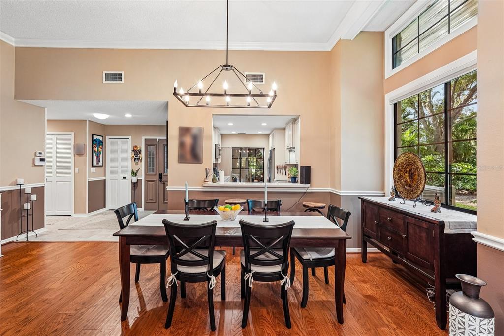 A dining room with a wooden table, chandelier, and a pass-through window to the kitchen — 5676 PIPERS WAITE UNIT 56, SARASOTA, FL
