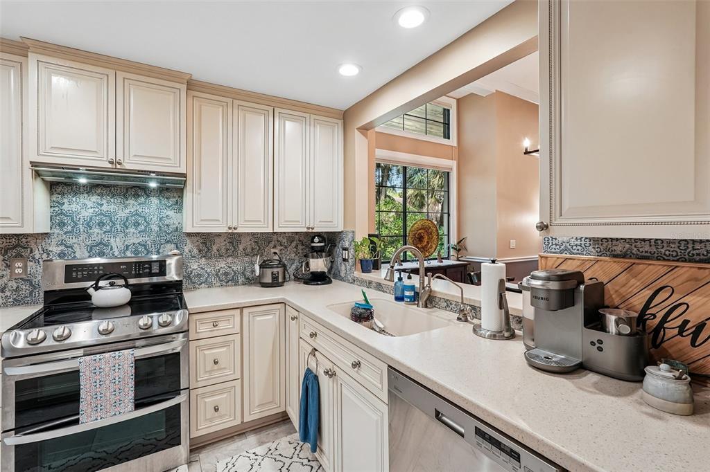 A kitchen features cream-colored cabinets, a patterned blue backsplash, stainless steel appliances, and quartz countertops — 5676 PIPERS WAITE UNIT 56, SARASOTA, FL
