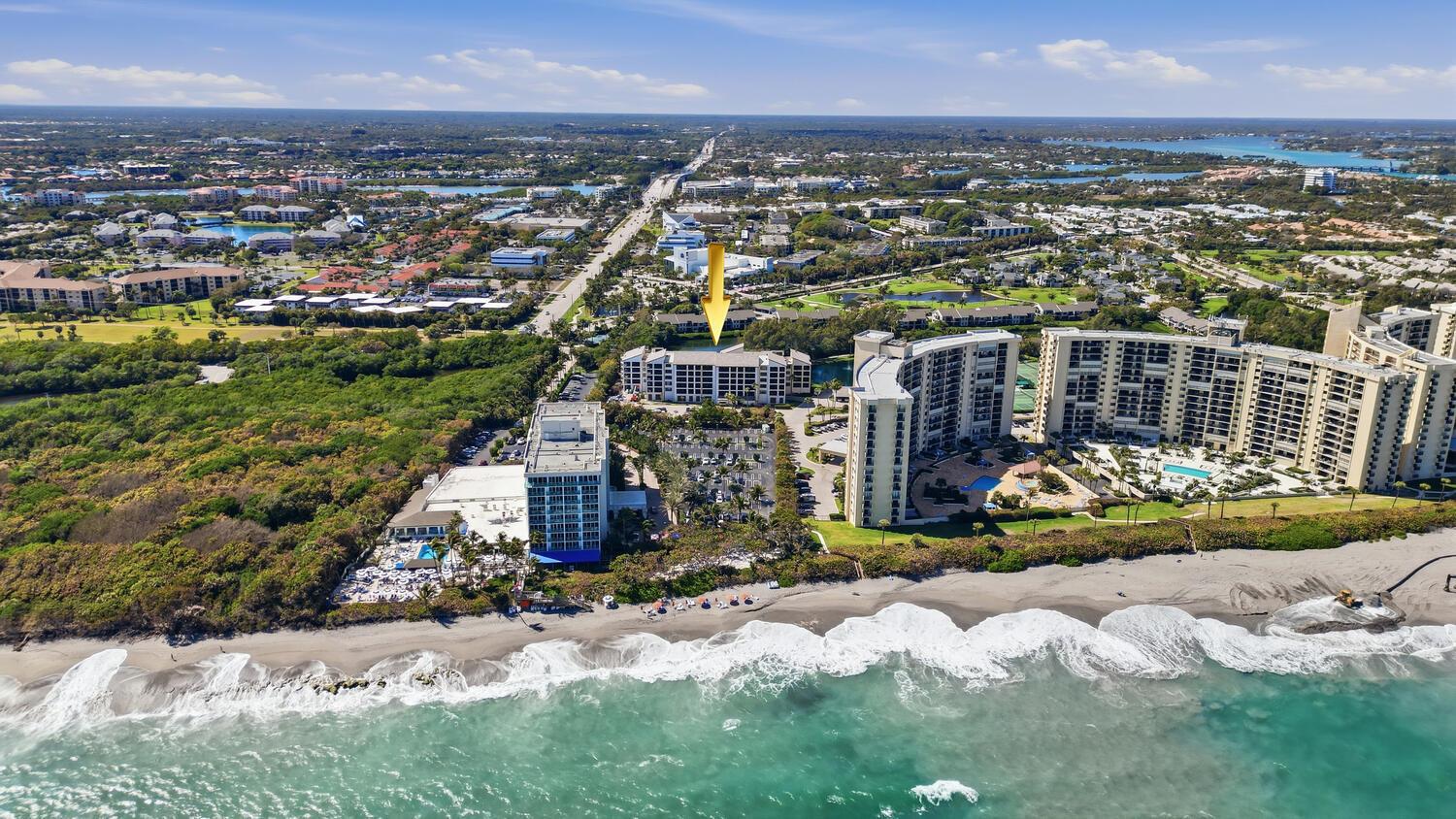 Aerial view of beachfront high-rise condominiums and surrounding coastal landscape with a yellow arrow marker — 500 Ocean Trail Way # 409, Jupiter FL 33477, JUPITER, FL