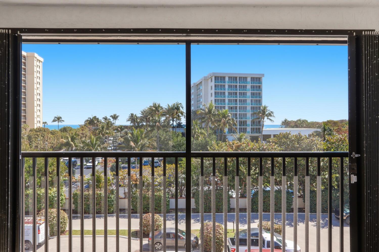 A view from a balcony looking out at palm trees, a parking lot, and oceanfront buildings — 500 Ocean Trail Way # 409, Jupiter FL 33477, JUPITER, FL