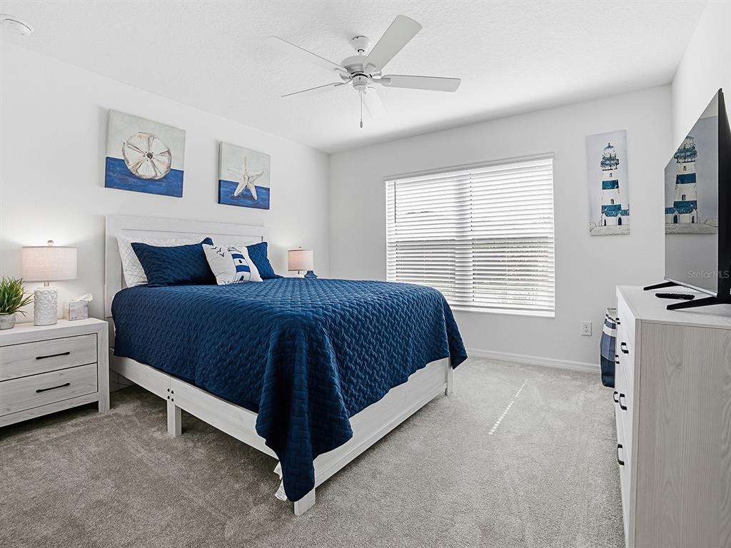 A bedroom features a blue quilt on a white bed frame, light wood furniture, and coastal-themed art — 7274 CARLOS COURT, THE VILLAGES, FL