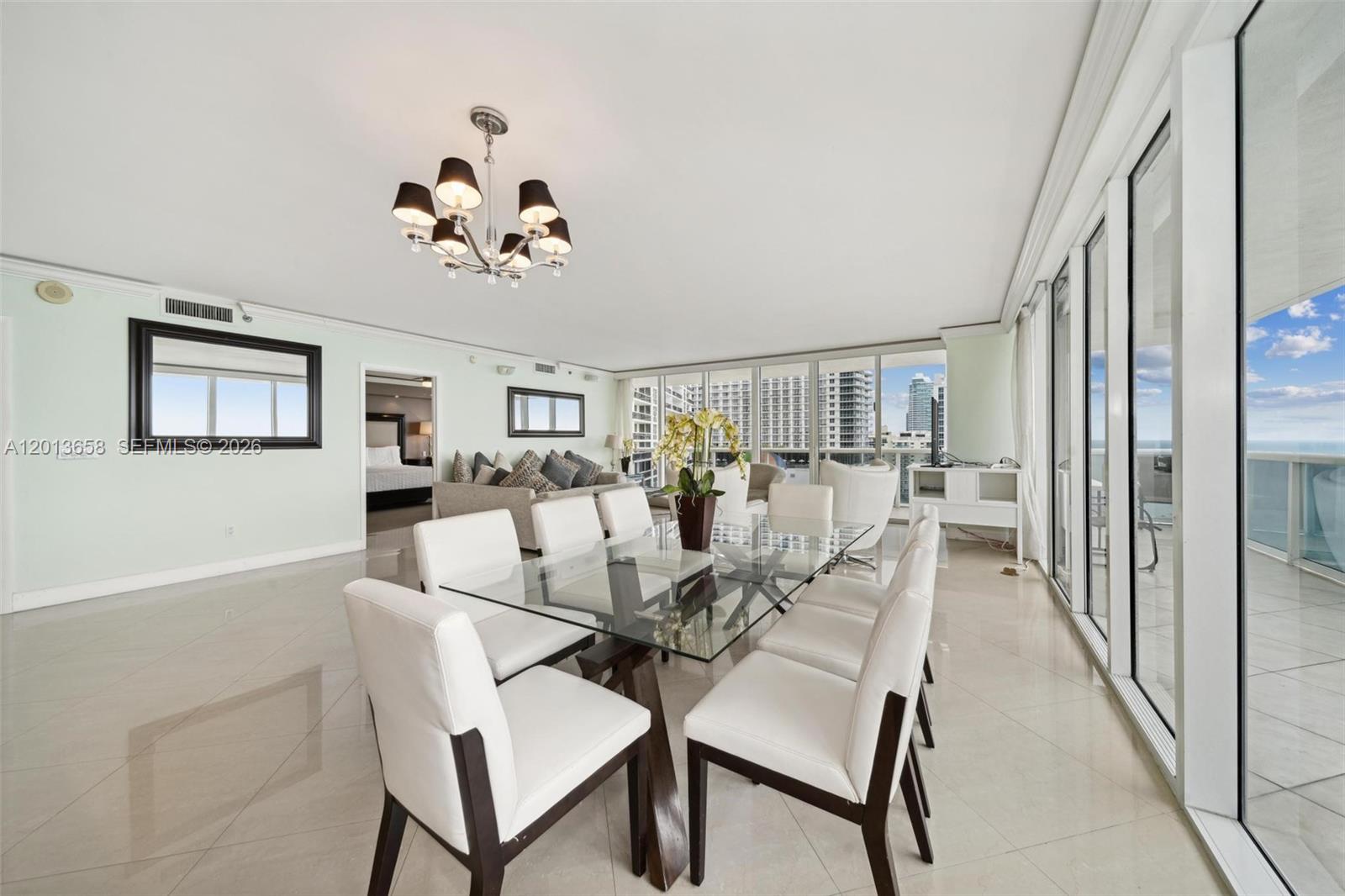 A dining area with a glass table and white chairs features floor-to-ceiling windows overlooking buildings — 1830 S Ocean Dr # 1701, Hallandale Beach FL 33009, HALLANDALE BEACH, FL