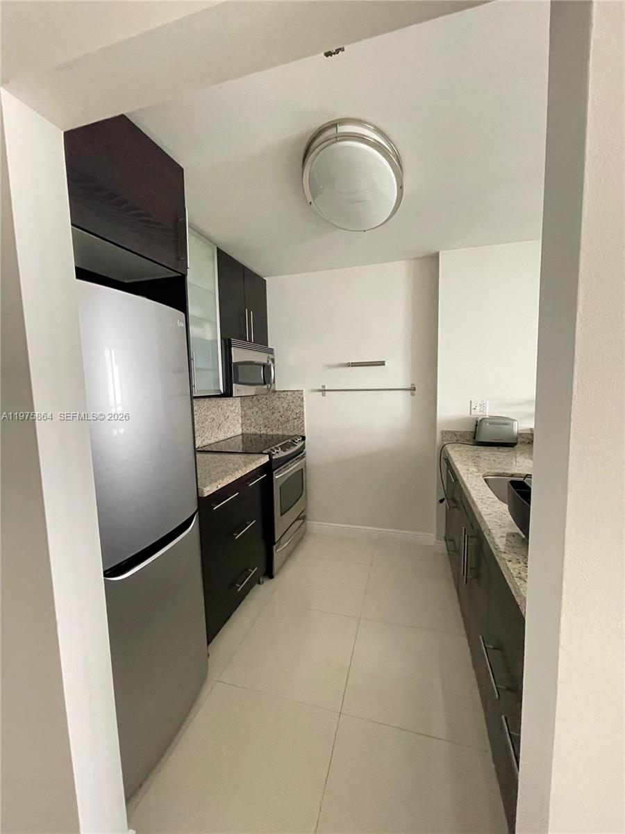 A galley kitchen features dark wood cabinets, stainless steel appliances, and light granite countertops — 800 N Miami Ave # 408, Miami FL 33136, MIAMI, FL