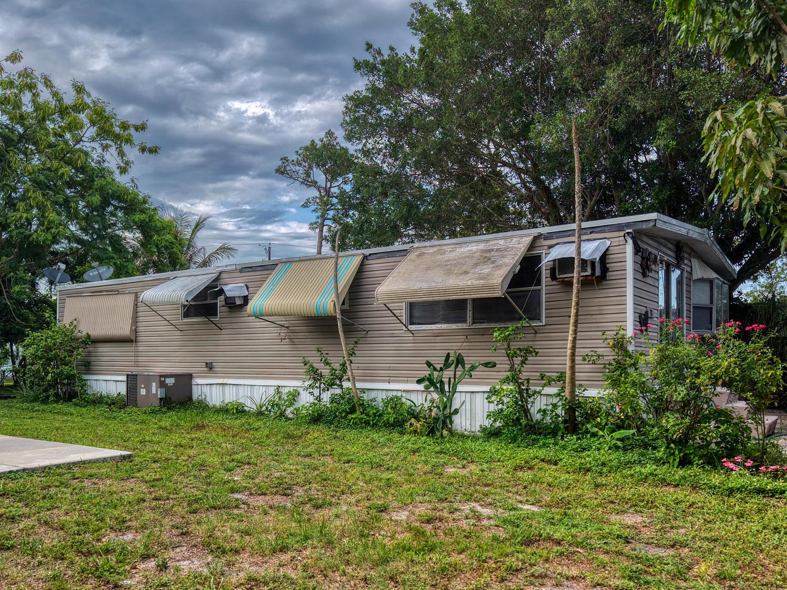 A single-wide mobile home with tan siding and striped window awnings sits on a lawn — 32 Lisa Lane, FL 33463, FL