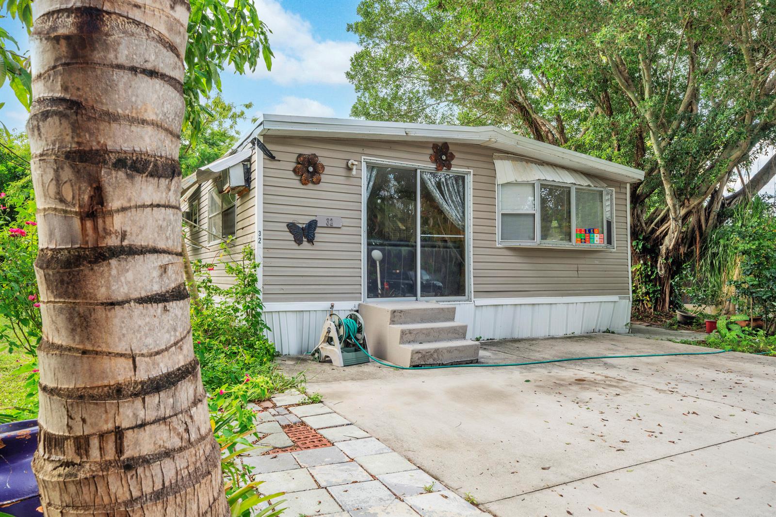 A beige mobile home with a sliding glass door, concrete steps, and a paved driveway — 32 Lisa Lane, FL 33463, FL