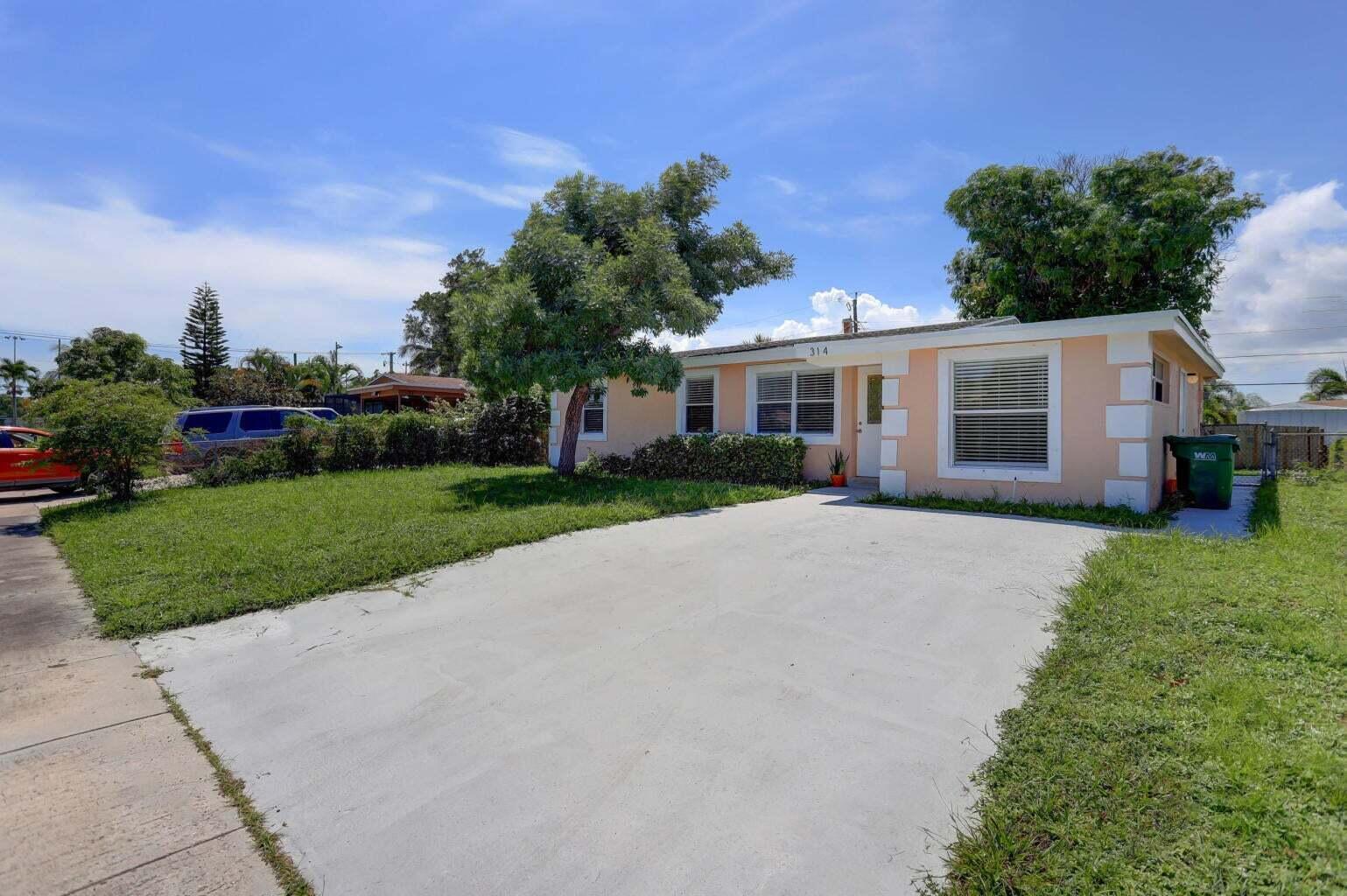 A single-story peach-colored house with a concrete driveway and a front yard under blue skies — 314 NW 12th Avenue, Delray Beach FL 33444, DELRAY BEACH, FL