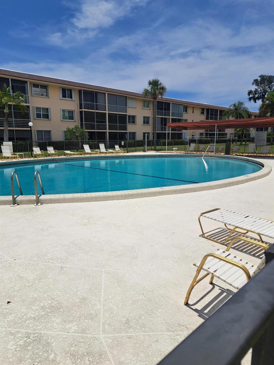 A swimming pool sits in front of a multi-story apartment building with screened balconies — 4502 N Federal Highway # D, Lighthouse Point FL 33064, LIGHTHOUSE POINT, FL