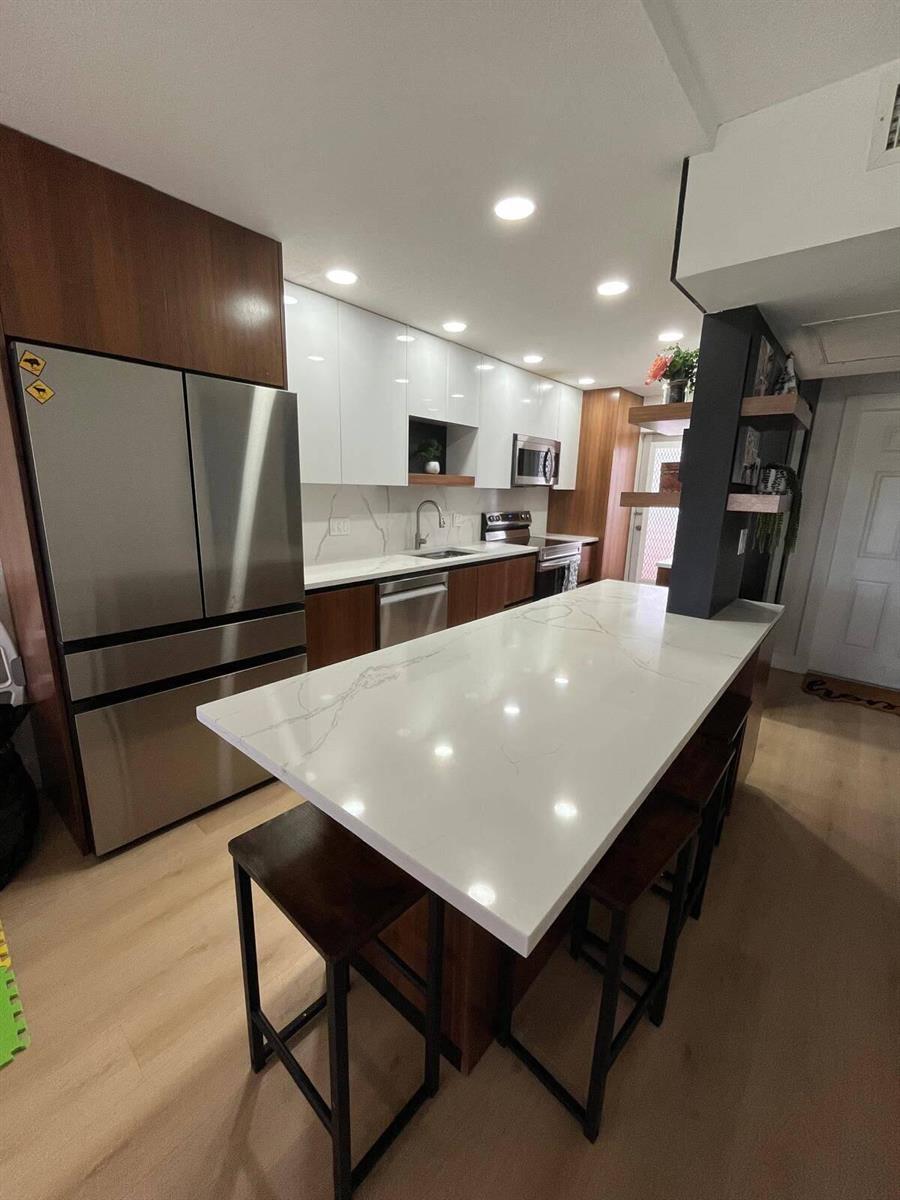 A modern kitchen features white upper cabinets, wood lower cabinets, a quartz island, and stainless appliances — 4502 N Federal Highway # D, Lighthouse Point FL 33064, LIGHTHOUSE POINT, FL