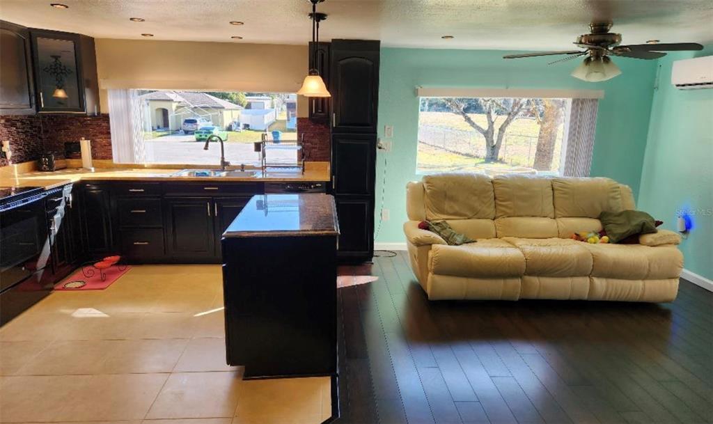 A kitchen with dark cabinets and an island opens into a living room with seating — 6371 FRANK COURT, BROOKSVILLE, FL
