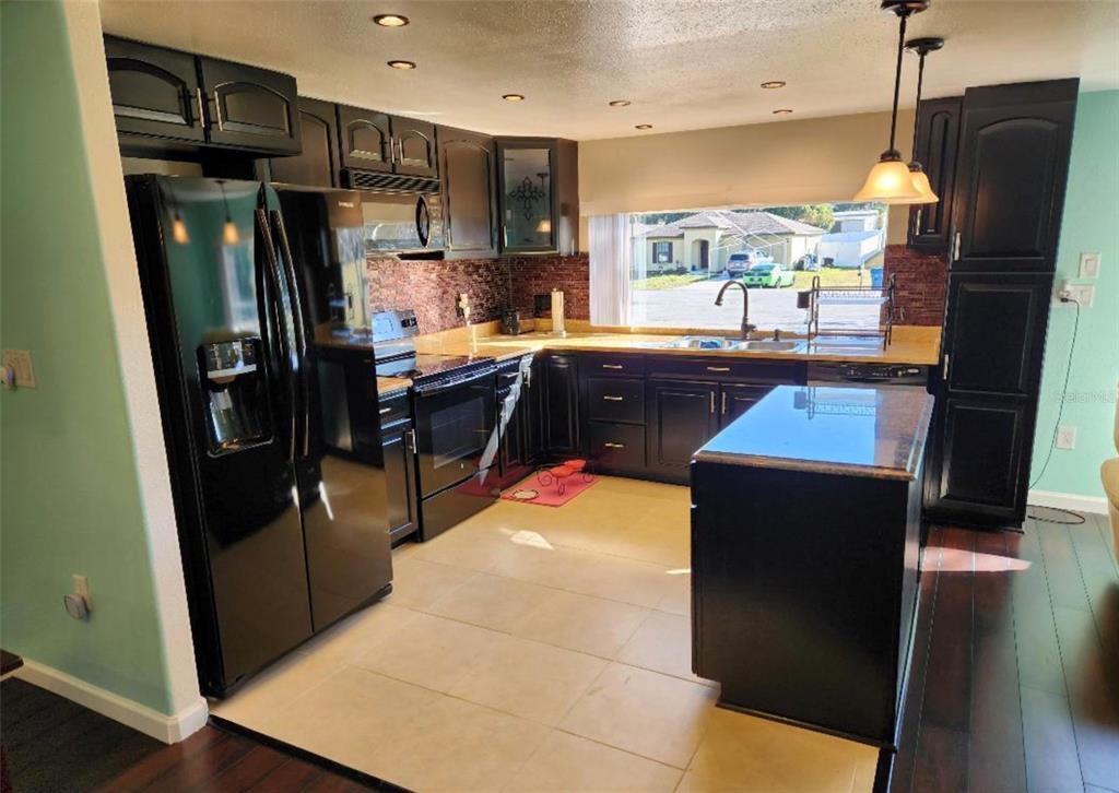 A kitchen features dark cabinetry, black appliances, a central island, and a tiled backsplash — 6371 FRANK COURT, BROOKSVILLE, FL