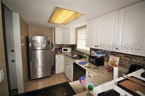 A kitchen features white cabinets, stainless steel appliances, and a stone-tiled backsplash — 1000 S SEMORAN BOULEVARD UNIT 404, WINTER PARK, FL