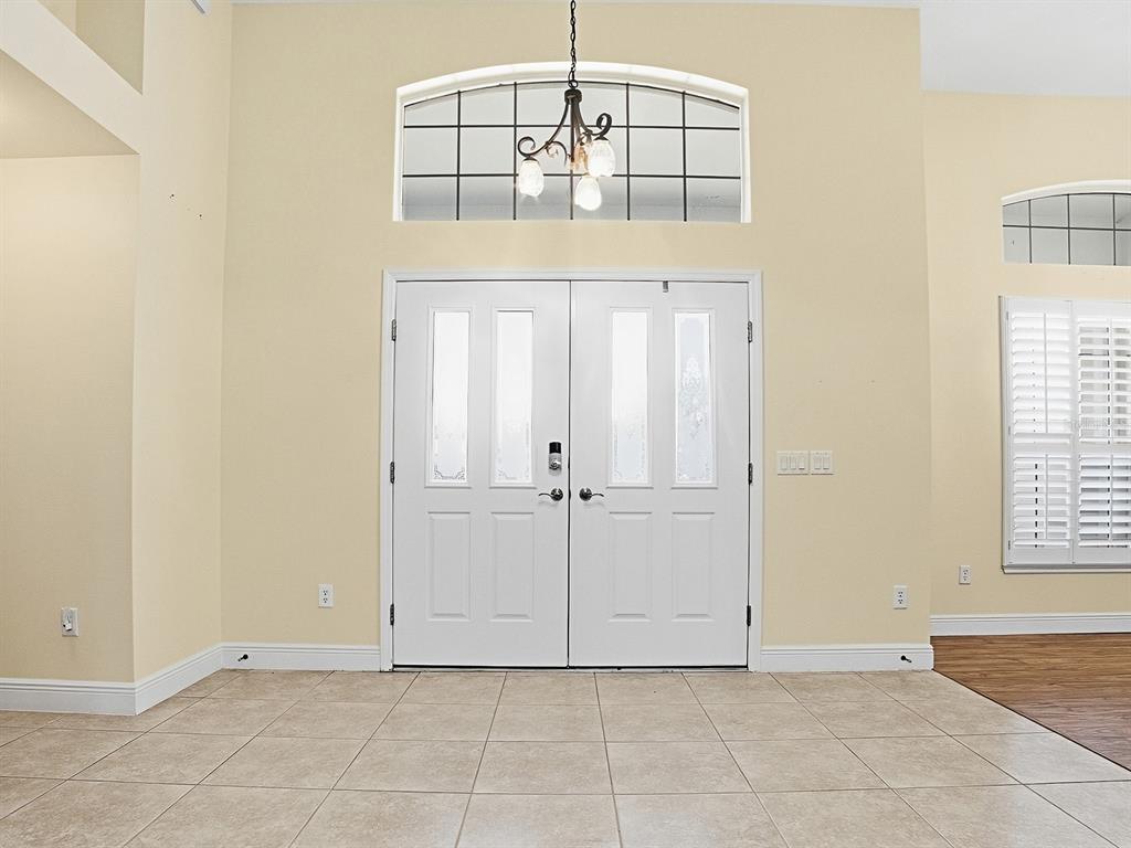 A foyer features double white doors, a transom window, a chandelier, and tiled flooring — 17627 SE 88TH COVINGTON CIRCLE, THE VILLAGES, FL