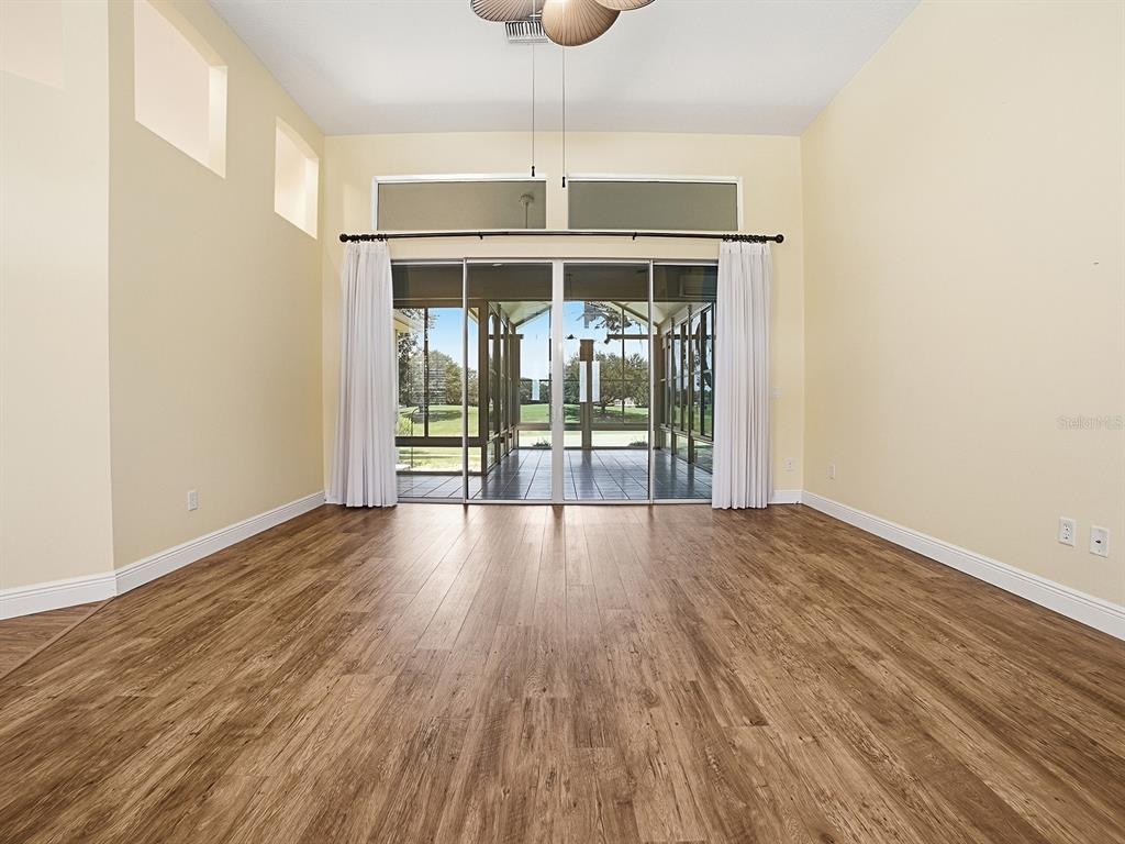 An empty room with wood-look flooring, high ceilings, and sliding glass doors leading to a lanai — 17627 SE 88TH COVINGTON CIRCLE, THE VILLAGES, FL