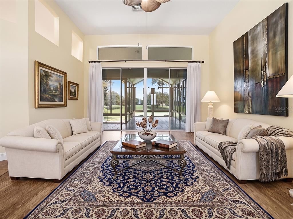 A living room features two cream sofas, a large blue patterned rug, and glass sliding doors — 17627 SE 88TH COVINGTON CIRCLE, THE VILLAGES, FL
