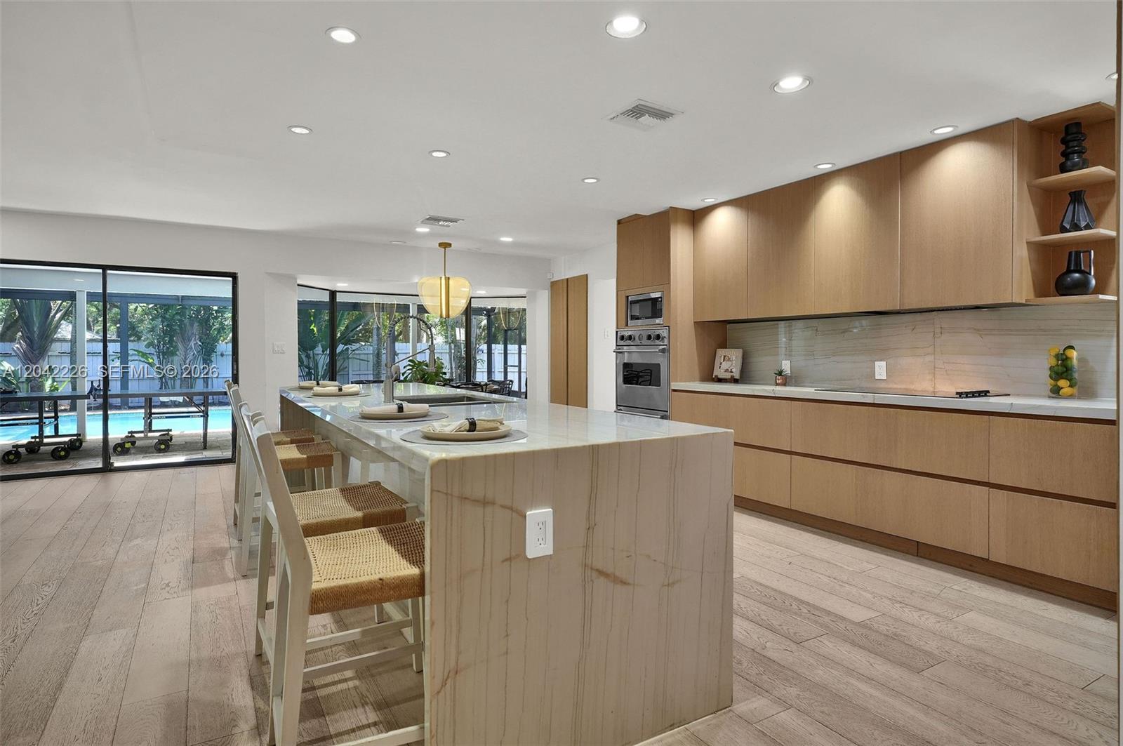 A modern kitchen features light wood cabinetry, a stone waterfall island, and views of a pool — 5801 SW 37th Ter, Dania Beach FL 33312, DANIA BEACH, FL
