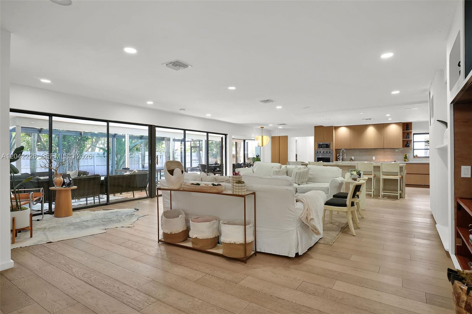 An open-concept living room features light wood flooring, white furniture, and large sliding glass doors — 5801 SW 37th Ter, Dania Beach FL 33312, DANIA BEACH, FL