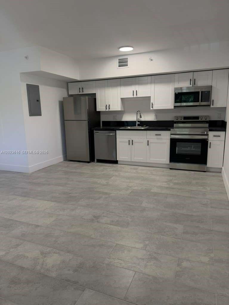 A modern kitchen features white cabinets, stainless steel appliances, and light gray tiled flooring — 147 Nw 59th St # 303, Miami FL 33127, MIAMI, FL
