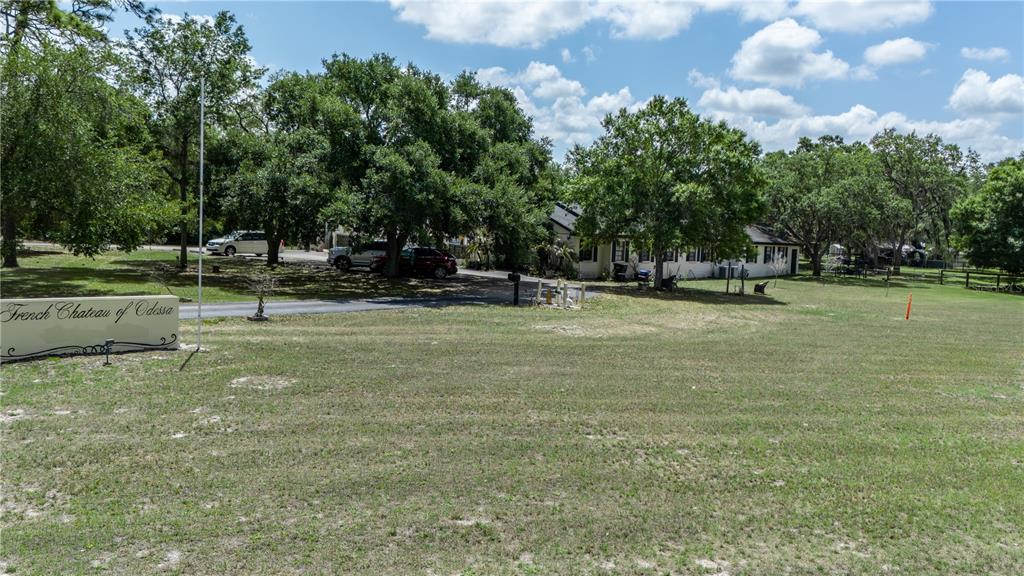 A grassy lot features a sign for French Chateau of Odessa and a distant house — 13042 TARPON SPRINGS ROAD, ODESSA, FL