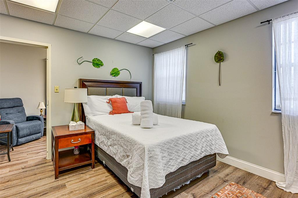 A bedroom features a bed with white linens, a wooden nightstand, and a blue recliner — 13042 TARPON SPRINGS ROAD, ODESSA, FL