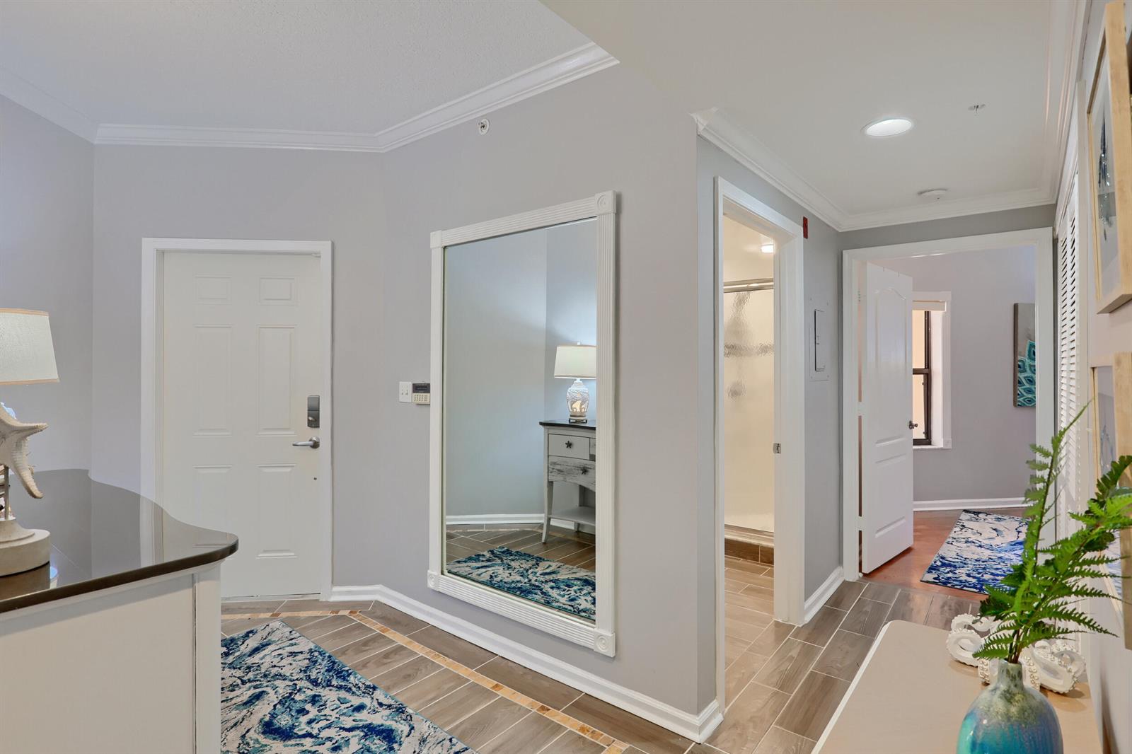 A hallway features light gray walls, tile flooring with blue patterned rugs, and a large mirror — 400 Uno Lago Drive # 204, Juno Beach FL 33408, JUNO BEACH, FL
