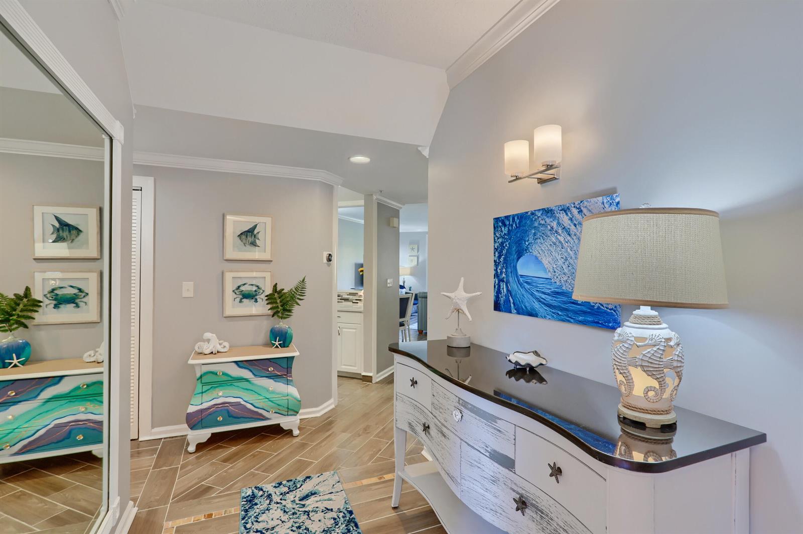 A coastal-themed hallway features a white console table, a colorful chest, and wood-look tile flooring — 400 Uno Lago Drive # 204, Juno Beach FL 33408, JUNO BEACH, FL