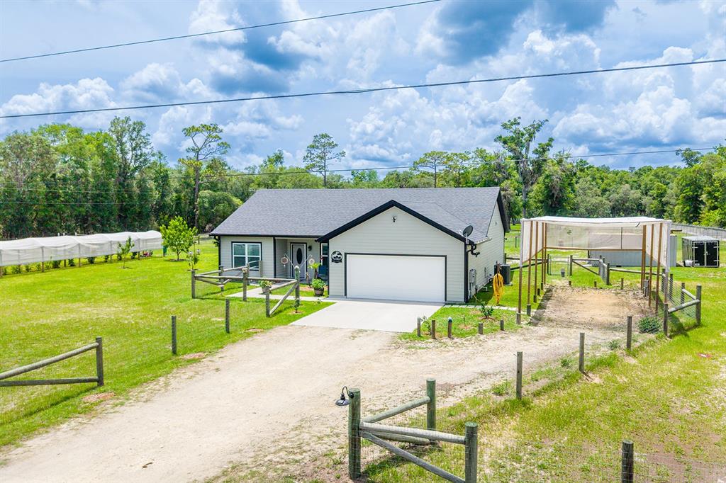 An exterior view of a single-story house with a garage, fenced yard, and greenhouse — 11030 NW 100TH AVENUE, CHIEFLAND, FL