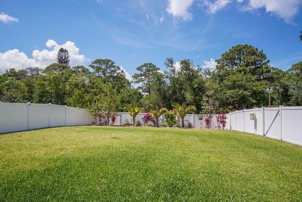 A grassy backyard enclosed by a white vinyl fence with trees in the background — 3909 SE Lee Street, Stuart FL 34997, STUART, FL