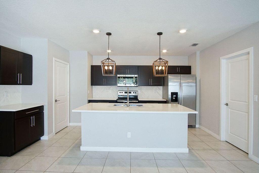 A kitchen features dark cabinets, white countertops, a central island, and two hanging pendant lights — 3909 SE Lee Street, Stuart FL 34997, STUART, FL