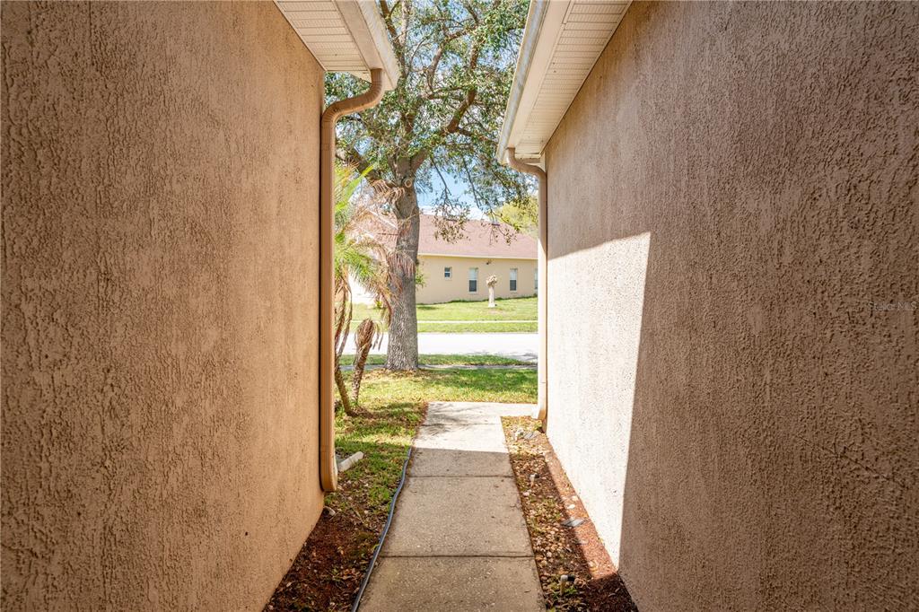 A narrow concrete walkway leads between two stucco exterior walls toward a grassy yard — 2563 ASTER COVE LANE, KISSIMMEE, FL