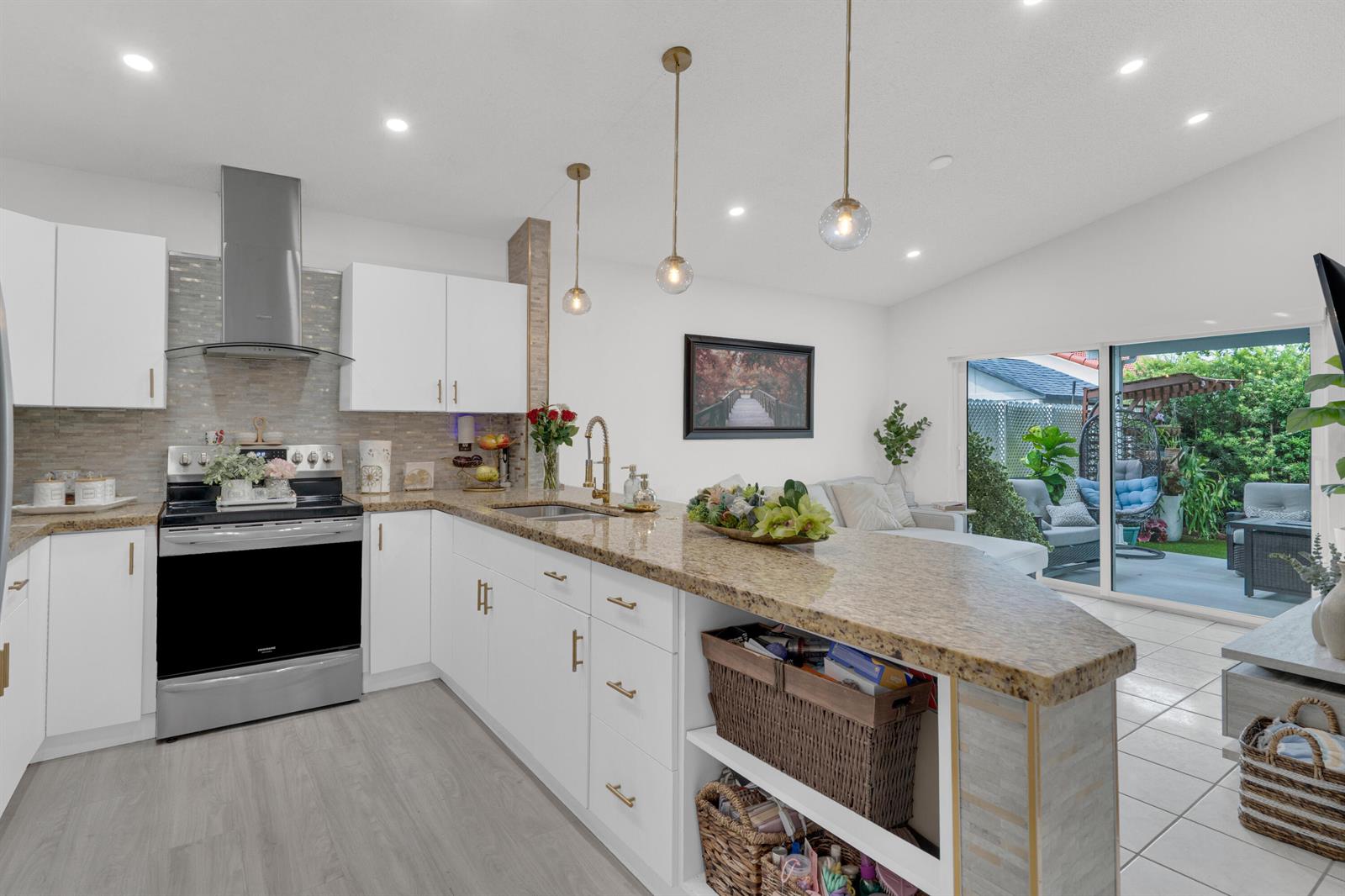 A kitchen with white cabinets, granite countertops, and a peninsula island opens to a patio — 17901 SW 144th Avenue, Miami FL 33177, MIAMI, FL