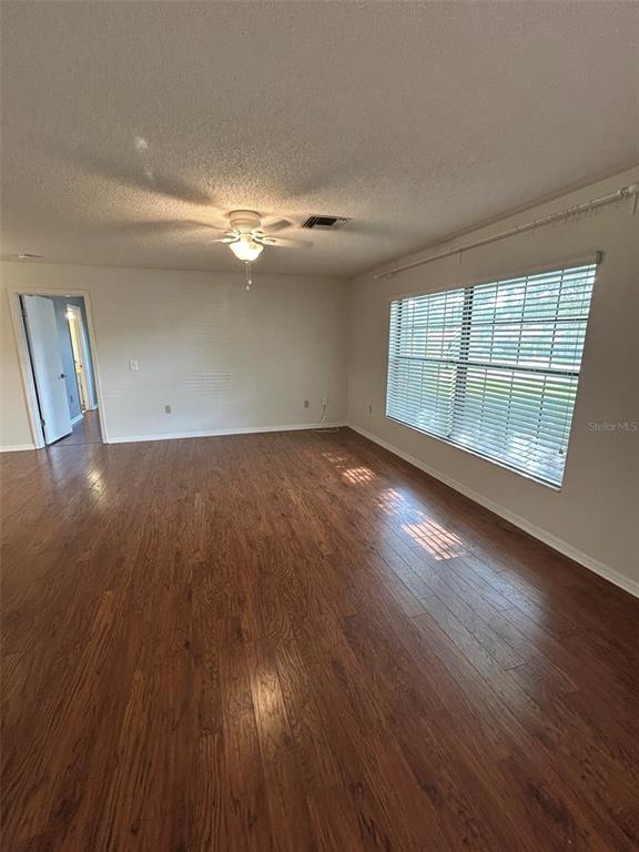 An empty room features wood-look flooring, a ceiling fan, and a large window with blinds — 1605 BLACKBERRY COURT, EUSTIS, FL