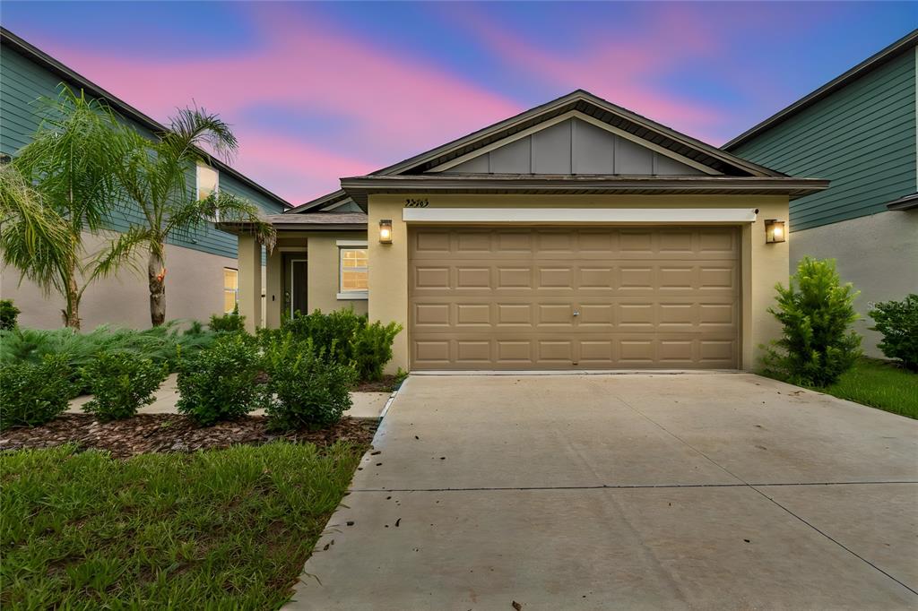 A single-story suburban house features a tan stucco exterior, a two-car garage, and landscaping — 22465 STORYBOOK CABIN WAY, LAND O LAKES, FL
