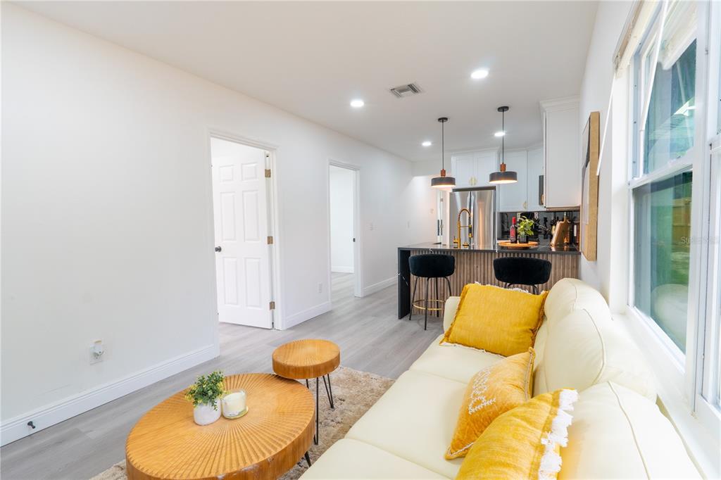 A living room with a white sofa and yellow pillows opens into a modern kitchen — 8408 N SEMINOLE AVENUE, TAMPA, FL