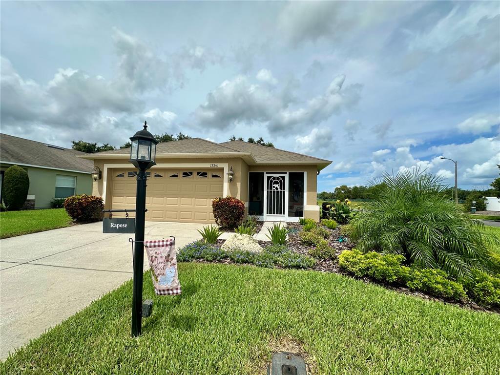 A single-story house with a tan stucco exterior, a two-car garage, and a landscaped front yard — 18861 WATER LILY LANE, HUDSON, FL