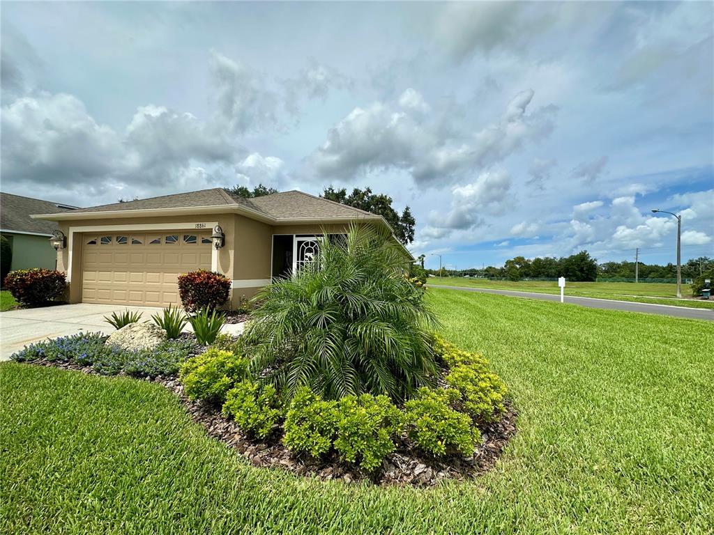 A single-story house with a tan exterior, a two-car garage, and a landscaped front yard — 18861 WATER LILY LANE, HUDSON, FL