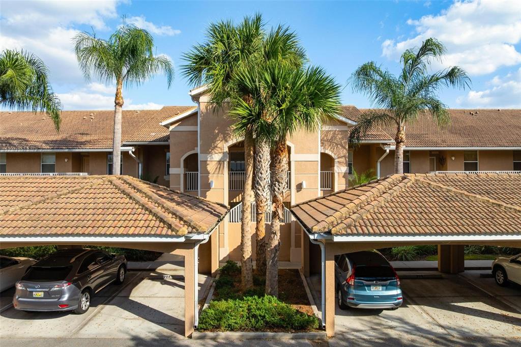 A two-story apartment building with covered parking spaces and palm trees in the foreground — 915 FAIRWAYCOVE LANE UNIT 204, BRADENTON, FL