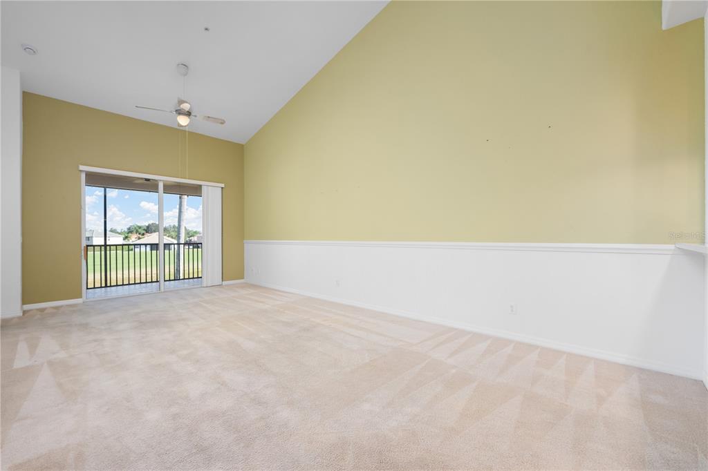 An empty living room features vaulted ceilings, beige carpeting, and a sliding glass door — 915 FAIRWAYCOVE LANE UNIT 204, BRADENTON, FL