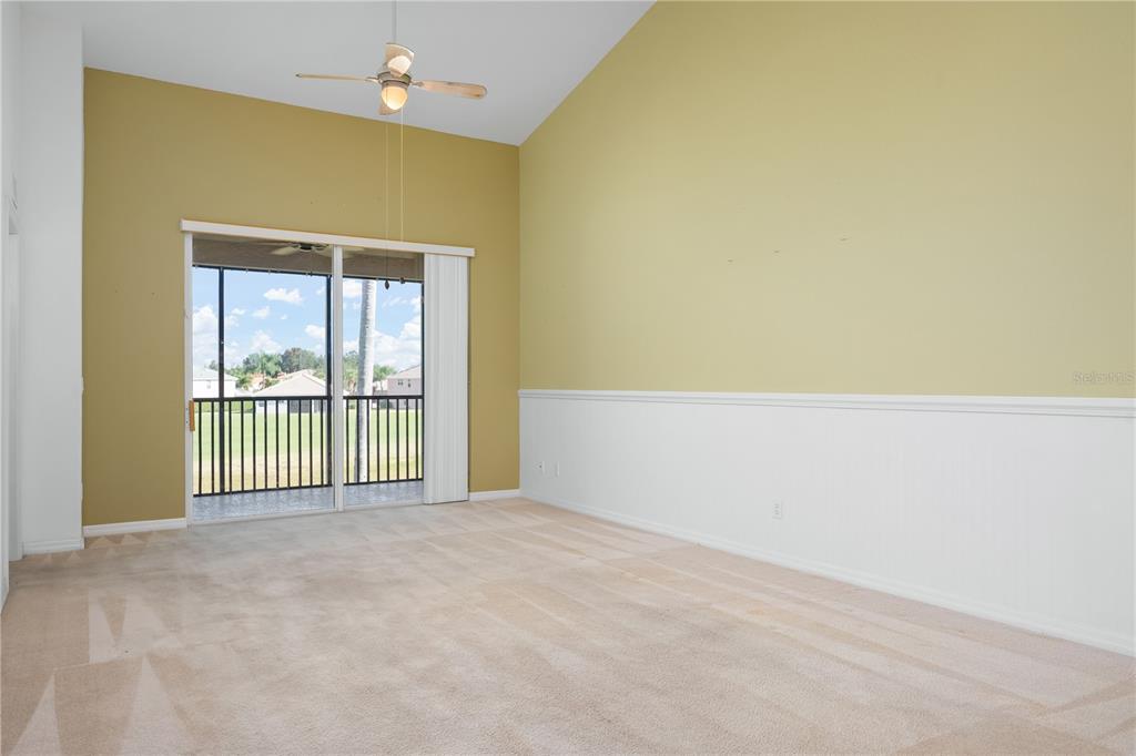 A living room with beige carpet, vaulted ceilings, a ceiling fan, and a sliding glass door — 915 FAIRWAYCOVE LANE UNIT 204, BRADENTON, FL