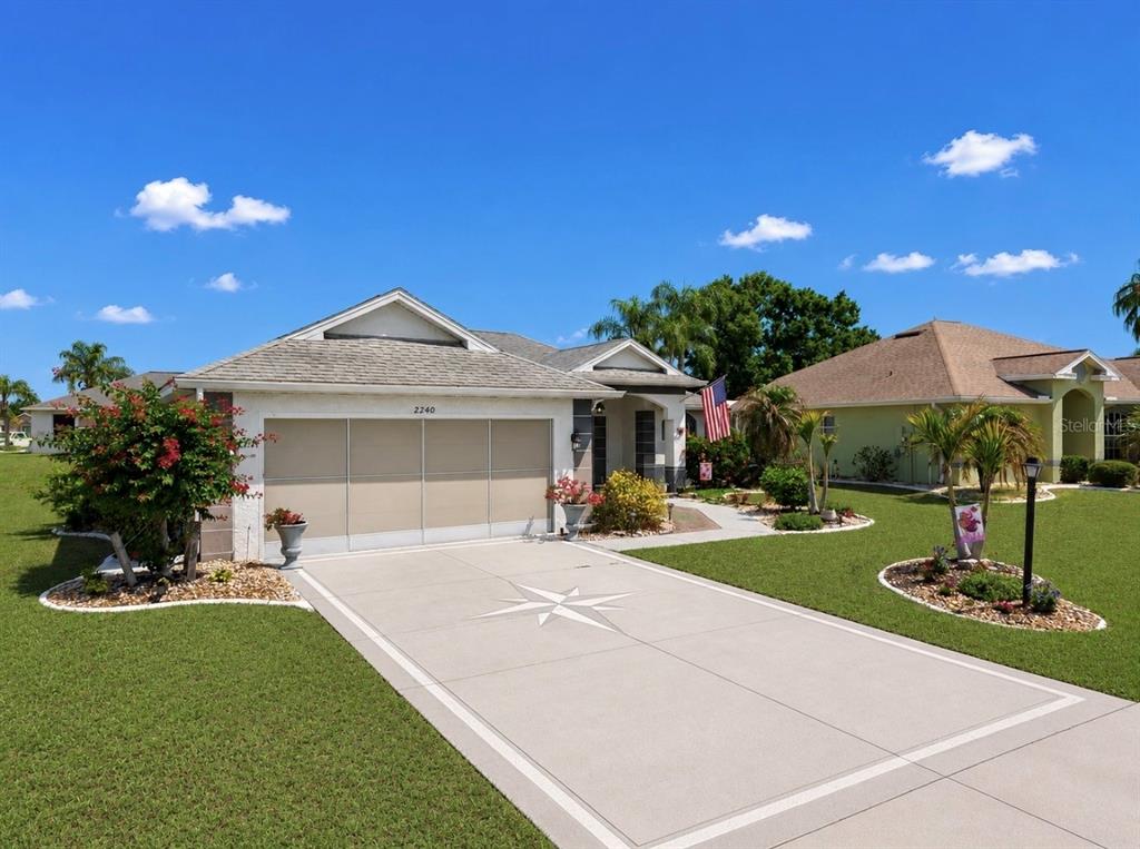 A single-story house with a beige garage door, a compass rose driveway, and a lawn — 2240 W DEL WEBB BOULEVARD UNIT 163, SUN CITY CENTER, FL