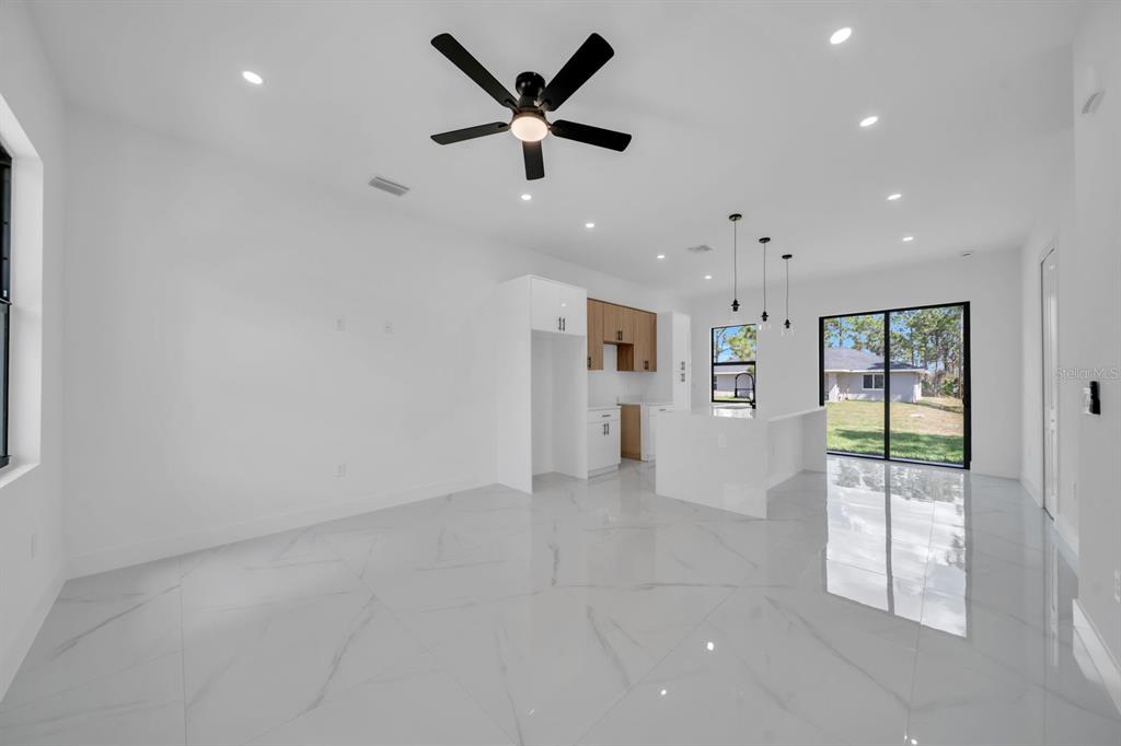 A bright, open-concept living and kitchen area features white marble-style tile flooring and recessed lighting — 635 SUMMIT AVENUE S, LEHIGH ACRES, FL